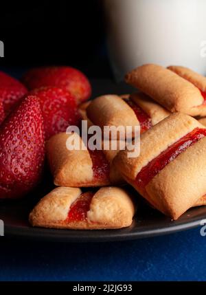 Une pile de barres à biscuits aux fraises avec un verre de lait froid et des fraises naturelles fraîches sur le côté de la nourriture sombre Banque D'Images