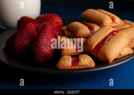 Une pile de barres à biscuits aux fraises avec un verre de lait froid et des fraises naturelles fraîches sur le côté de la nourriture sombre Banque D'Images