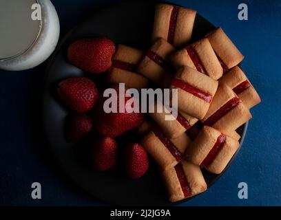 Une pile de barres à biscuits aux fraises avec un verre de lait froid et des fraises naturelles fraîches sur le côté de la nourriture sombre Banque D'Images