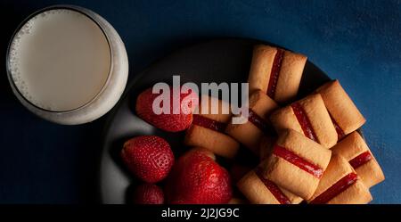 Une pile de barres à biscuits aux fraises avec un verre de lait froid et des fraises naturelles fraîches sur le côté de la nourriture sombre Banque D'Images