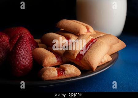 Une pile de barres à biscuits aux fraises avec un verre de lait froid et des fraises naturelles fraîches sur le côté de la nourriture sombre Banque D'Images