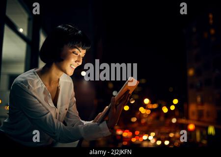 Rester dans le savoir tout au long de la nuit. Prise de vue d'une jeune femme attirante utilisant une tablette numérique à l'extérieur de la ville la nuit. Banque D'Images