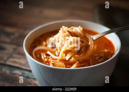 Soupe mexicaine de nouilles chaude à la tomate avec de l'ail à l'oignon et d'autres condiments, dans un bol blanc, sur une ancienne table en bois, Banque D'Images