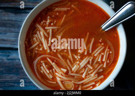 Soupe mexicaine de nouilles chaude à la tomate avec de l'ail à l'oignon et d'autres condiments, dans un bol blanc, sur une ancienne table en bois, Banque D'Images