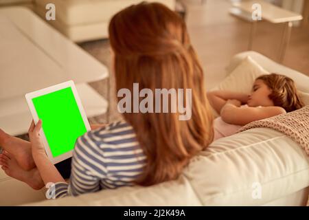 En ligne et en famille - le meilleur des deux mondes. Prise de vue d'une mère utilisant sa tablette à la maison pendant que sa fille dort. Banque D'Images