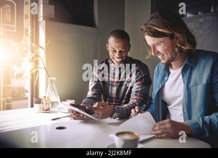 Le café nourrit leur créativité. Prise de vue de deux amis utilisant une tablette tout en prenant un café dans un café. Banque D'Images