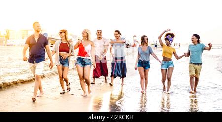 Grand groupe d'amis heureux branchés marchant à la plage à l'heure du coucher du soleil - concept multiracial de style de vie avec les jeunes s'amuser pendant les vacances d'été - Banque D'Images