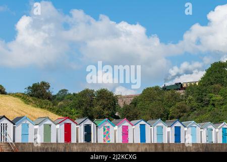 Maisons de plage colorées. Rangée de cabanes de plage multicolores avec train à vapeur d'époque sur viaduc de pierre contre ciel bleu. Banque D'Images