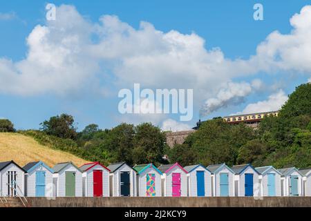 Maisons de plage colorées. Rangée de cabanes de plage multicolores avec train à vapeur d'époque sur viaduc de pierre contre ciel bleu. Banque D'Images