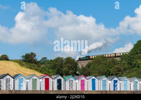 Maisons de plage colorées. Rangée de cabanes de plage multicolores avec train à vapeur d'époque sur viaduc de pierre contre ciel bleu. Banque D'Images