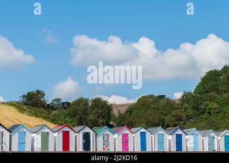 Maisons de plage colorées. Rangée de cabanes de plage multicolores avec train à vapeur d'époque sur viaduc de pierre contre ciel bleu. Banque D'Images
