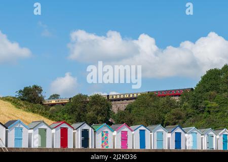 Maisons de plage colorées. Rangée de cabanes de plage multicolores avec train à vapeur d'époque sur viaduc de pierre contre ciel bleu. Banque D'Images