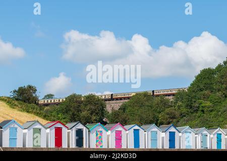 Maisons de plage colorées. Rangée de cabanes de plage multicolores avec train à vapeur d'époque sur viaduc de pierre contre ciel bleu. Banque D'Images