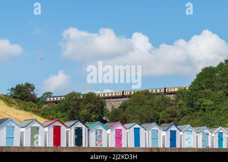Maisons de plage colorées. Rangée de cabanes de plage multicolores avec train à vapeur d'époque sur viaduc de pierre contre ciel bleu. Banque D'Images