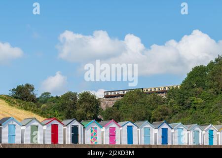 Maisons de plage colorées. Rangée de cabanes de plage multicolores avec train à vapeur d'époque sur viaduc de pierre contre ciel bleu. Banque D'Images