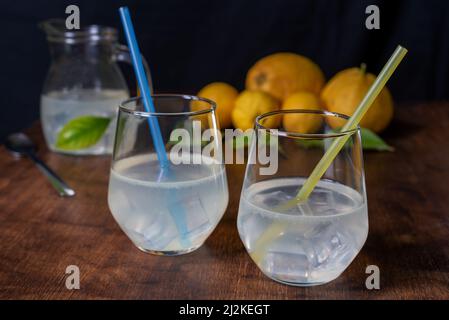 Deux verres de limonade avec pailles, derrière un citron et un pichet à fond noir. Banque D'Images