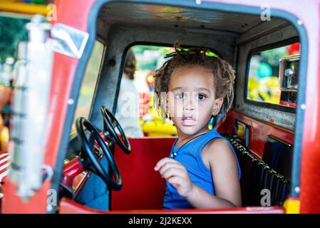 Petit garçon mixte de race enfant jouant sur un carrousel, jeune garçon prétendant conduire une voiture, concept de diversité et de race mixte, génération de l'Africain et Banque D'Images