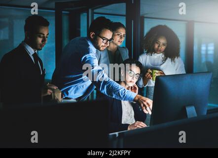 Cela prend plus de temps que nous ne le pensions. Prise de vue de collègues se tenant ensemble lorsqu'ils travaillent sur un ordinateur la nuit. Banque D'Images