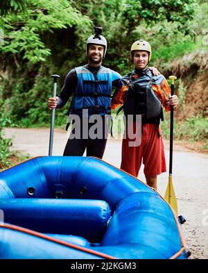 C'est ce que nous avons fait depuis que nous étions des enfants. Portrait de deux jeunes hommes joyeux portant un équipement de protection tout en tenant une paddle pour aller au rafting en rivière. Banque D'Images