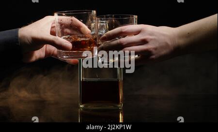 Deux mains avec des verres de whisky cognac et des glaçons pour faire des cheers toast sur fond noir Banque D'Images