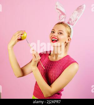 Fille de Pâques dans les oreilles de lapin peignant des œufs. Lapin femme avec oeuf de couleur et pinceau. Banque D'Images