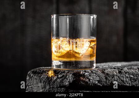 Verre doré de whisky avec glace sur planches brûlées. Whisky sur des rochers sur une table brûlée. Banque D'Images