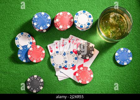 Table verte pour le poker avec whisky, cartes et jetons. Verre de bourbon avec glace sur table de jeu avec cartes et jetons. Banque D'Images