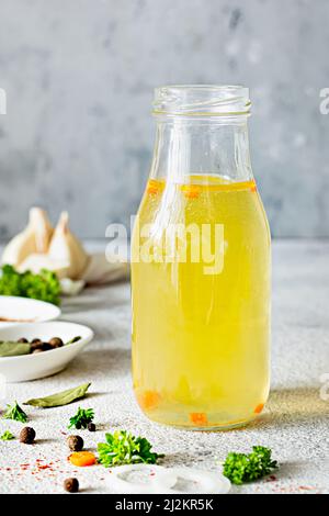 Bouillon de poulet (os) maison (bouillon) avec légumes, épices et herbes dans une bouteille en verre sur fond clair. Collagène naturel d'origine animale. Banque D'Images