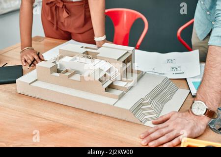 Concevoir leurs rêves fait partie de la tâche. Gros plan de deux architectes travaillant ensemble sur un modèle d'échelle d'un bâtiment dans un bureau. Banque D'Images