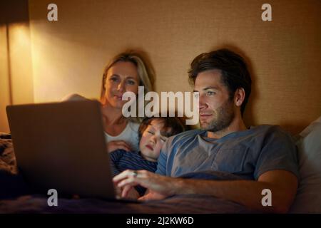 Vous êtes en train de vous départir pour rêver tout en regardant des films. Une jeune famille allongé dans un lit et regardant un écran d'ordinateur portable. Banque D'Images