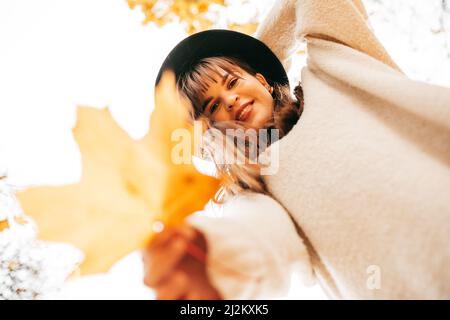 Portrait souriant belle femme regardant vers le bas de l'appareil photo, tenant la feuille d'érable doré de près. Activités de loisirs. Angle bas Banque D'Images