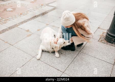 Femme, propriétaire de chien, se promener, embrasser et jouer avec l'animal Golden Labrador retriever sur la rue en pierre. Formation Banque D'Images