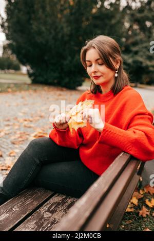 Portrait vertical d'une jolie étudiante de femme réfléchie, assise sur un banc, tenir le bouquet de feuilles d'érable. Parc nature automnale Banque D'Images