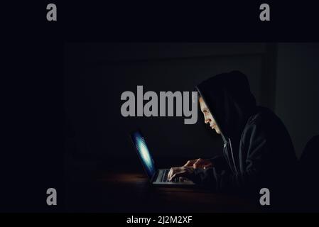 S'aider à vos mots de passe. Photo d'un pirate informatique à capuchon utilisant un ordinateur portable dans le noir. Banque D'Images
