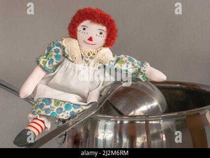 Raggedy Ann se trouve sur la poignée d'une bouilloire avec une louche de soupe à proximité. C'est un gros plan d'une petite poupée avec pot de cuisine comme elle joue dans la cuisine. Banque D'Images
