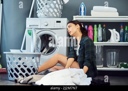 Je préfère faire QUOI que ce soit d'autre en ce moment Prise de vue d'une jeune femme attrayante qui a l'air de s'ennuyer tout en faisant le linge à la maison. Banque D'Images