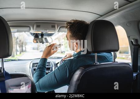 Un homme adulte mâle caucasien boire de l'alcool à partir de la fiole tout en conduisant une voiture ivre vue arrière copie espace alcoolisme et abus d'alcool concept ivre Banque D'Images