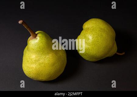 Deux poires vertes mûres sur fond sombre, variété de poires fin novembre. Fruits entiers Banque D'Images
