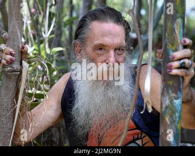 L'ancien mâle caucasien spirituel mystique avec la longue barbe grise et les ongles peints a l'air amical et accueillant de la jungle au spectateur. Banque D'Images