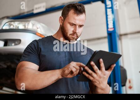 Ouvrez l'application pour trouver un mécanicien fiable et digne de confiance près de chez vous. Photo d'un mécanicien utilisant une tablette numérique tout en travaillant dans un atelier de réparation automobile. Banque D'Images