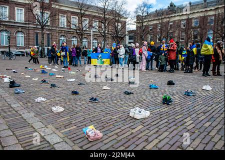 La Haye, pays-Bas. 02nd avril 2022. Chaussures disposées en rangées sur la plaine de Het, pendant que les adultes et les enfants drapaient dans les drapeaux ukrainiens et tiennent des écriteaux pendant la manifestation. Une installation artistique ukrainienne a été placée devant la Chambre des représentants des pays-Bas, pour attirer l'attention des autorités néerlandaises et de la population sur les meurtres de civils et en particulier d'enfants pendant la guerre en Ukraine. Crédit : SOPA Images Limited/Alamy Live News Banque D'Images