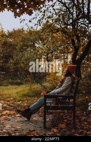 Jeune femme assise sur banc seule et regardant vers le haut en automne Banque D'Images