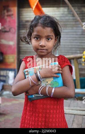 Une jeune fille à Mumbai, en Inde, vivant avec sa famille appauvrie sur un sentier (trottoir) à Kalbajevi Rd / Bhuleshwar, encombrant un livre scolaire Banque D'Images