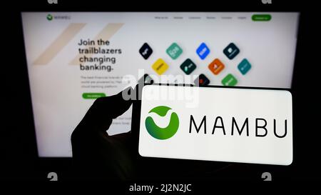 Personne tenant le téléphone portable avec le logo de la société fintech allemande Mambu GmbH sur l'écran en face de la page web d'affaires. Mise au point sur l'affichage du téléphone. Banque D'Images