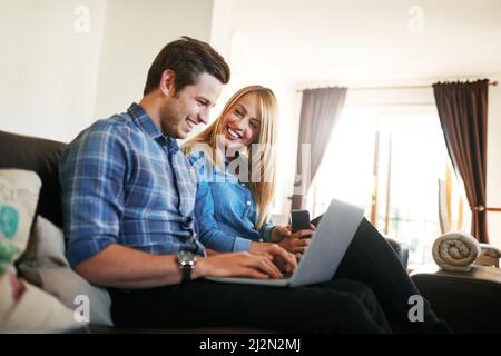 Passer quelques heures en ligne. Photo courte d'un jeune couple affectueux surfant sur le net tout en étant assis sur leur canapé à la maison. Banque D'Images