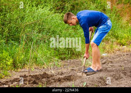 Le jeune homme creuse le sol avec une pelle dans le jardin, libère le sol pour la plantation de légumes. Maison potager dans la campagne Banque D'Images