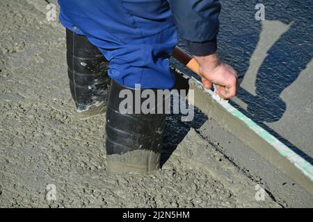 Un constructeur tient la cheville profondément dans le ciment humide pendant un versement de béton Banque D'Images