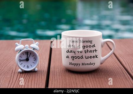 Réveil blanc sur parquet avec texte du matin sur une tasse de café - c'est une bonne journée pour commencer une bonne semaine. Avec un arrière-plan flou de la piscine. Banque D'Images