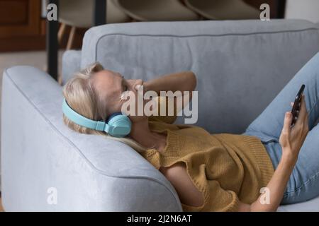 Bonne femme d'âge moyen dans un casque sans fil écoutant de la musique Banque D'Images