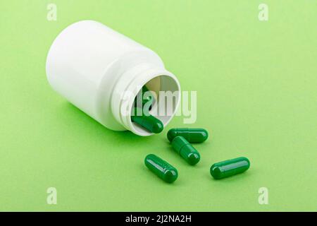 Capsules de médicaments versant d'une bouteille de pilule, fond vert. Banque D'Images